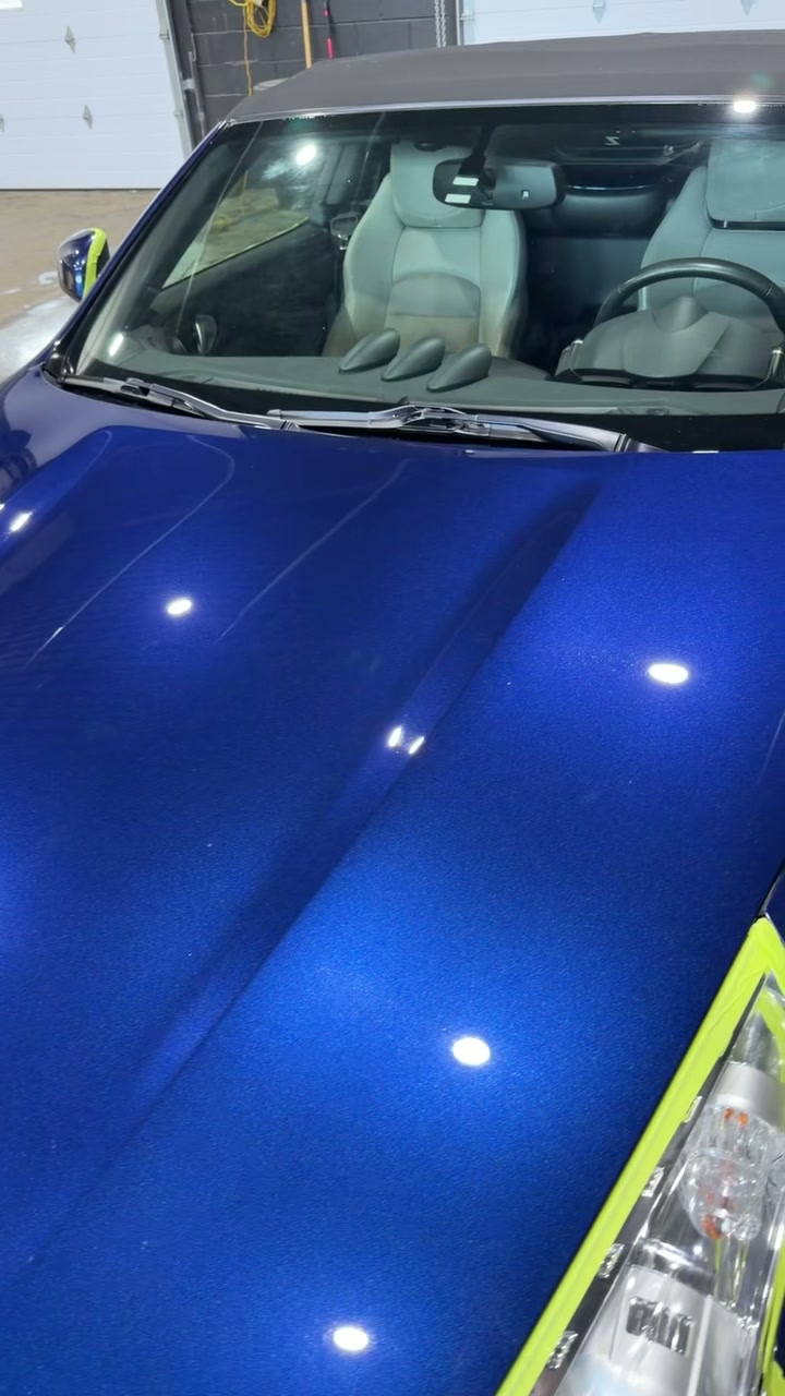 Blue Nissan hood with the headlight area masked off in the studio during ceramic coating.