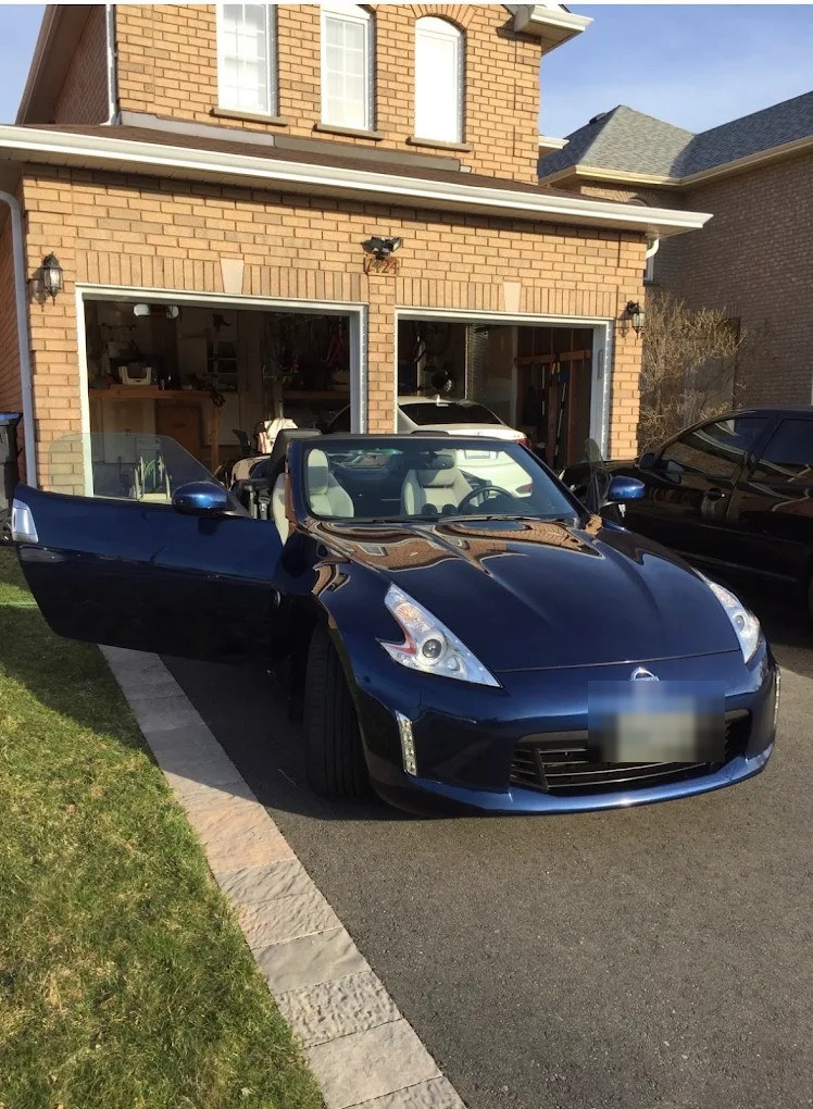 Blue Nissan convertible with a high-gloss finish in a driveway after ceramic coating. Plate blurred for privacy.